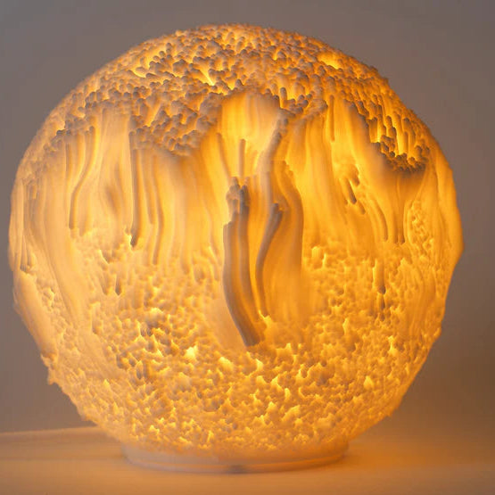 Decorative lamp with textured organic looking surface and warm glow on a plain background